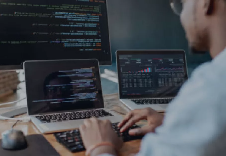 Two laptops and one large screen monitor is pictured with a person typing on one of the laptops.